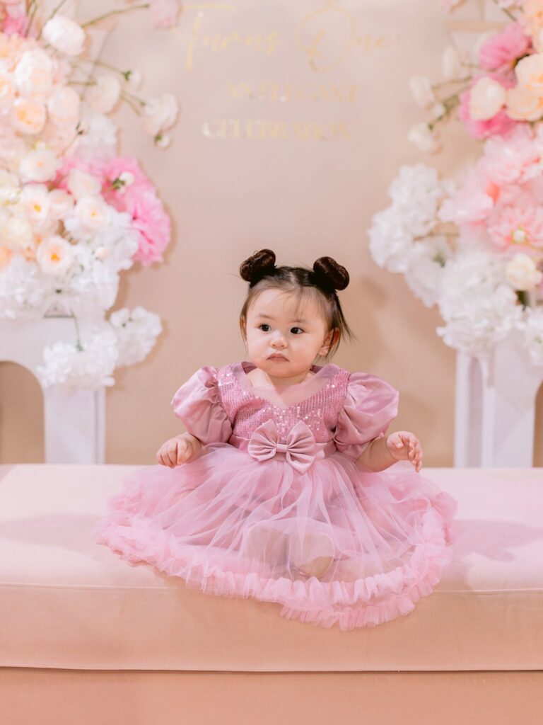 Girl in pink dress, floral backdrop.
